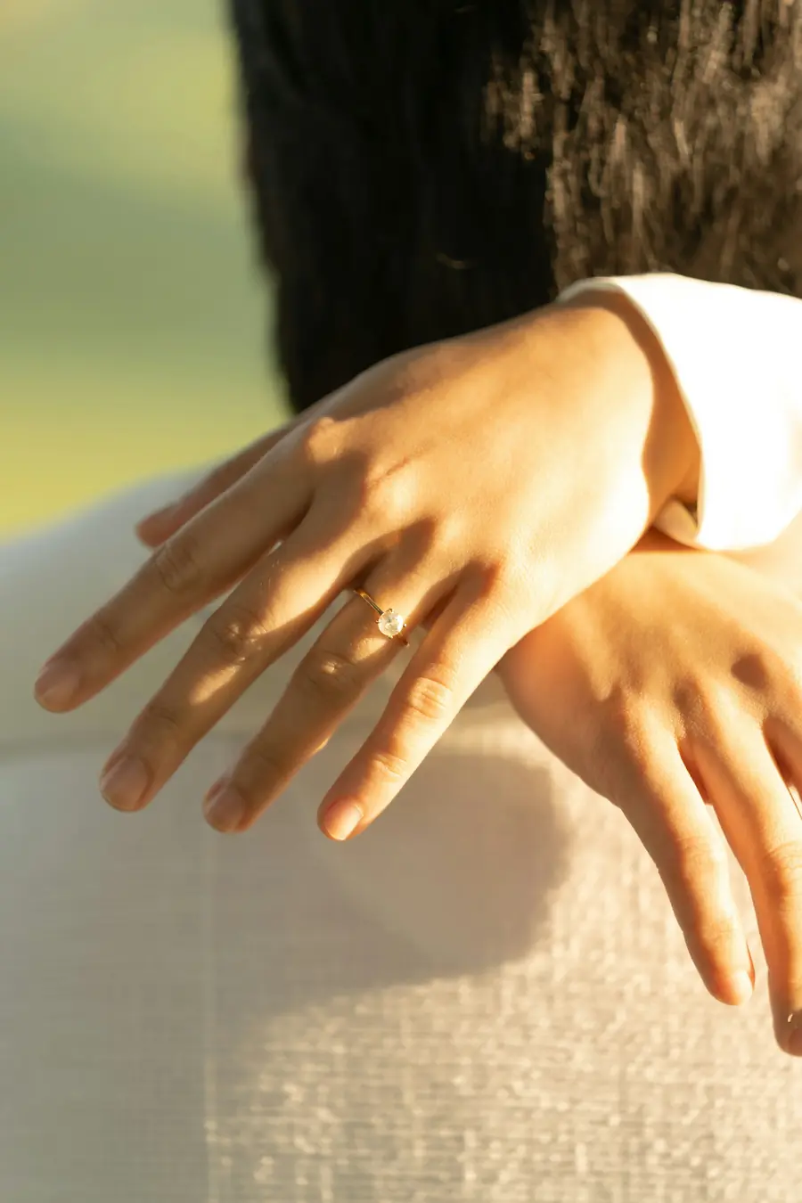 Two hands resting together, one wearing a solitaire diamond ring