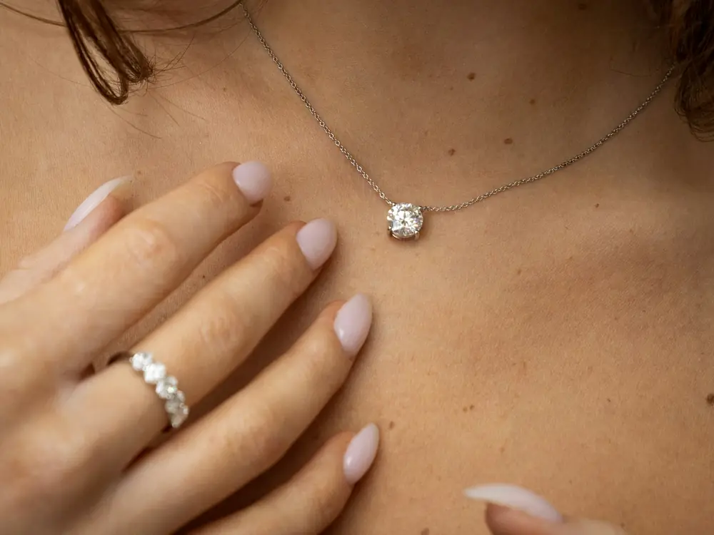 A hand resting below a round diamond solitaire pendant
