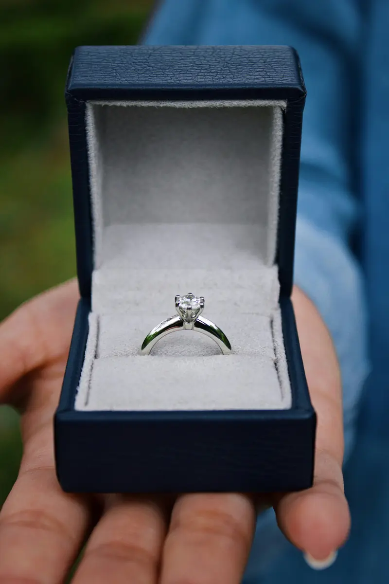 A solitaire diamond engagement ring in an open ring box, held in a hand
