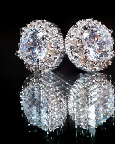 A pair of round halo diamond stud earrings on a black reflective surface